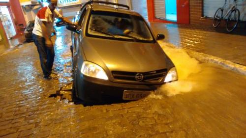 Calçamento cede com enxurradas e carro fica preso em buraco
